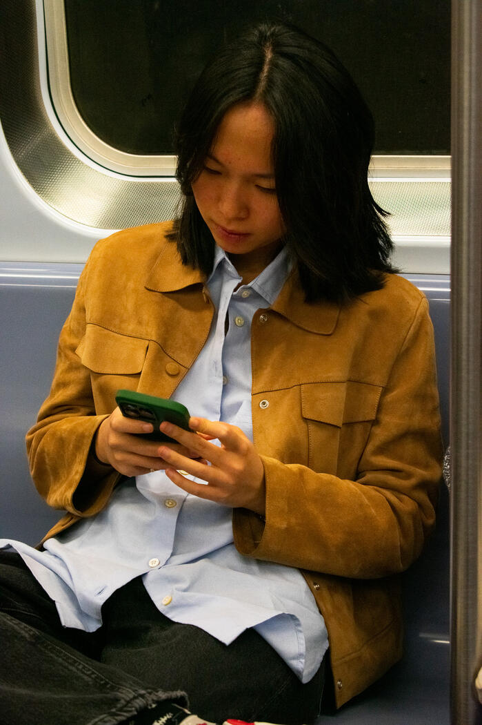 Young Asian woman on a New York subway train looking at her phone.